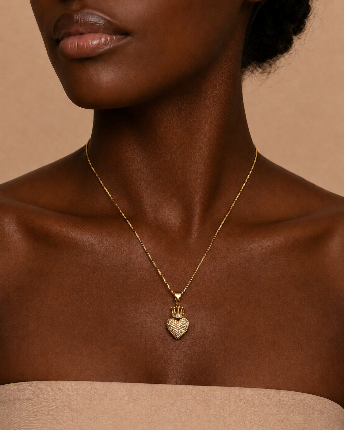 A close-up of a model wearing a delicate gold chain necklace with a textured heart-shaped pendant, set against a warm beige background.