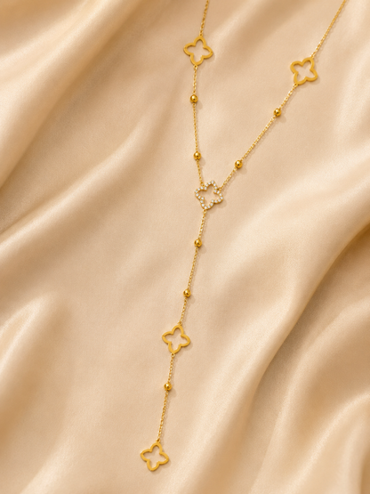 A delicate gold Y-shaped necklace with four star-shaped charms and small bead accents, displayed on a draped beige satin fabric.