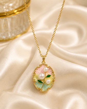A gold chain necklace with an oval pendant featuring a floral design in pastel pink, mint green, and white pearls, displayed on draped cream satin fabric.
