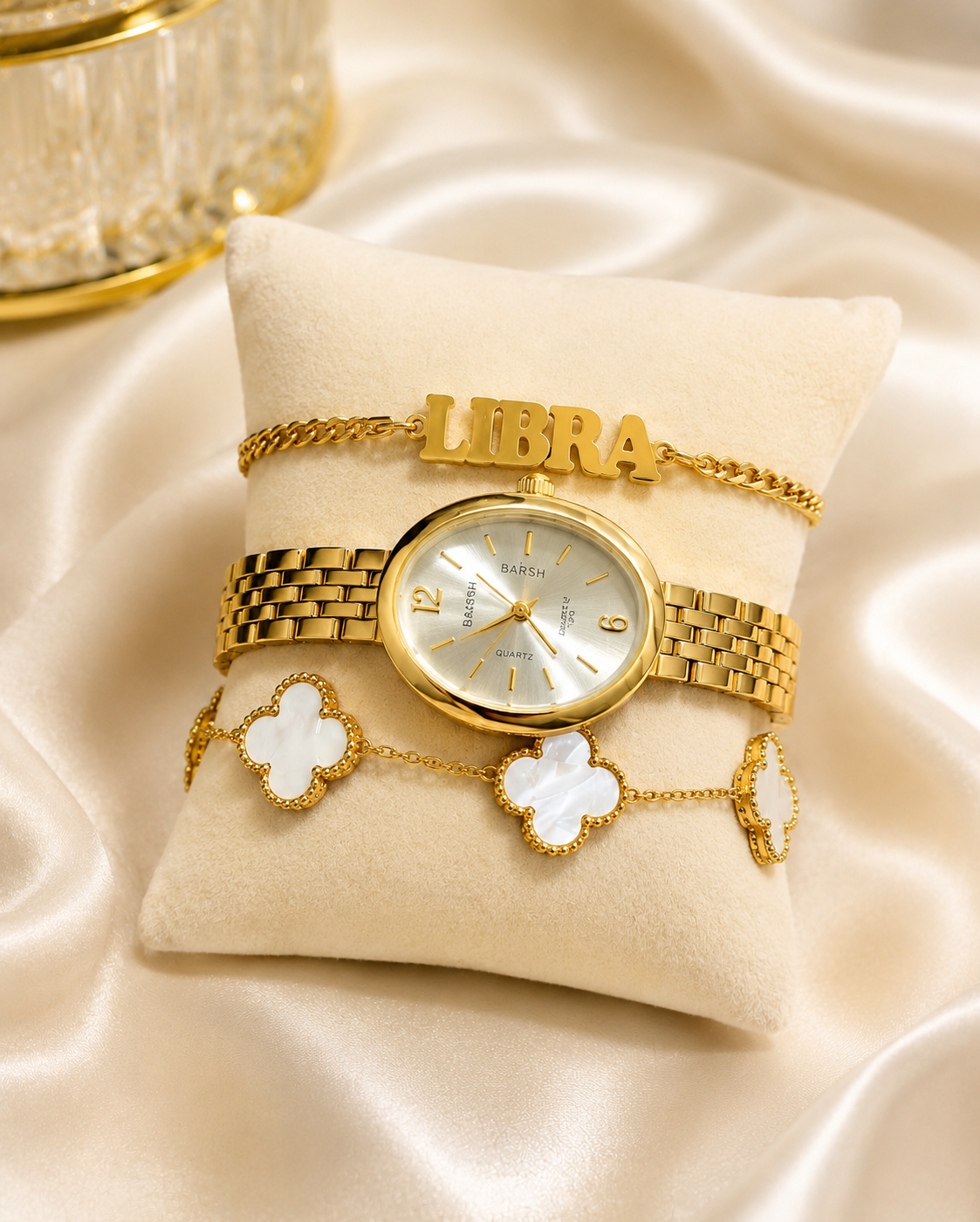 A gold-tone watch with a matching bracelet displayed on a cream-colored velvet cushion. The watch has a gold-tone metal case and bracelet, a white dial, and gold hour markers.